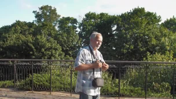 Viejo hombre camina cerca de barandilla de metal contra la exuberante naturaleza verde — Vídeos de Stock