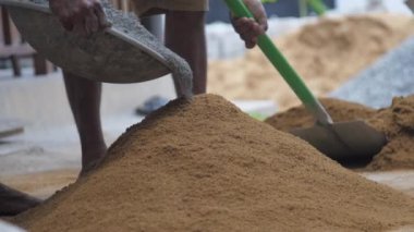 Biri sarı kumu kapar ve kürekle yığına atar.