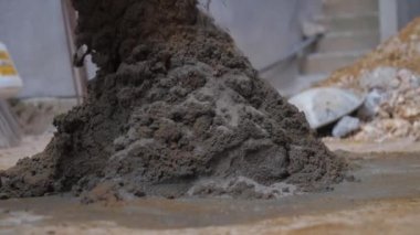 İnsan ıslak çimentoyla yerdeki metal küreği karıştırır.