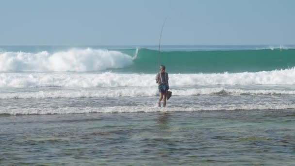 Local fisherman holds rod in hand in waving blue ocean — Stock Video