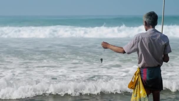 Рыбак держит удочку в руке и идет против океана — стоковое видео