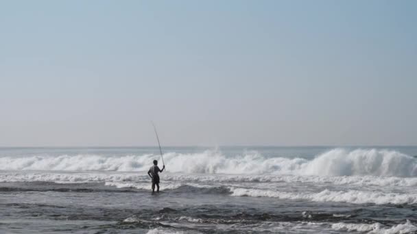 Local fisherman holds rod in hand in waving blue ocean — Stock Video