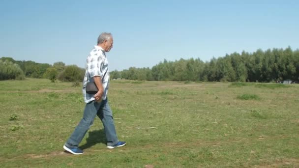 Pensionné actif en jeans marche le long de la pelouse verte activement — Video