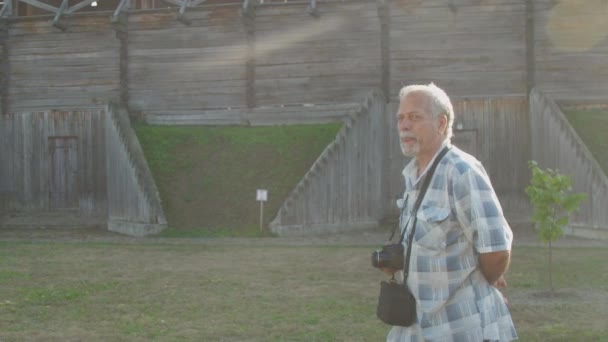 Homme aux cheveux gris marche et parle contre la forteresse en bois — Video