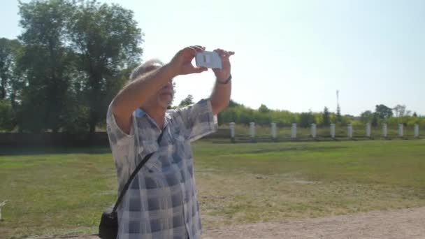 Пожилой человек держит в руках смартфон против музея поместья — стоковое видео