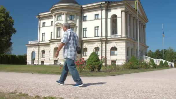 Gråhårig gammal man går längs grön park zon mot himlen — Stockvideo