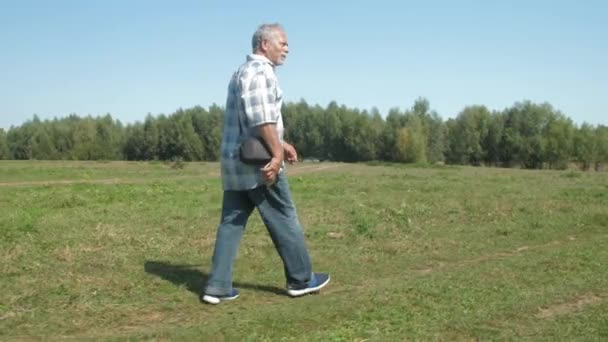 Активный пенсионер в джинсах активно ходит по зеленой лужайке — стоковое видео