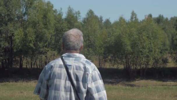 Pensionista activo en jeans camina a lo largo de césped verde activamente — Vídeos de Stock