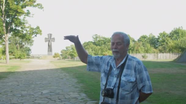 Grey haired man walks and speaks against wooden fortress — Stock Video