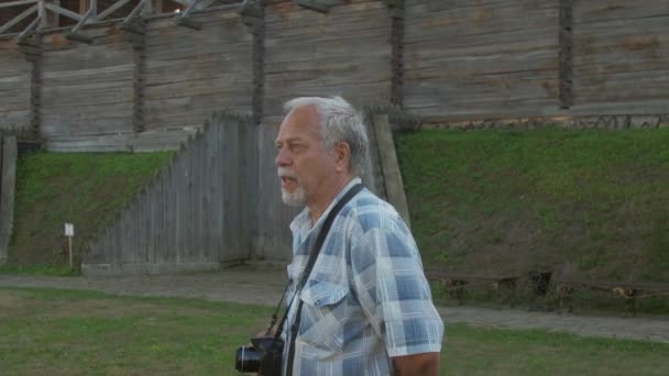 Homme aux cheveux gris marche et parle contre la forteresse en bois — Video