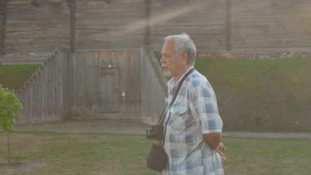 Uomo dai capelli grigi cammina e parla contro fortezza di legno — Video Stock