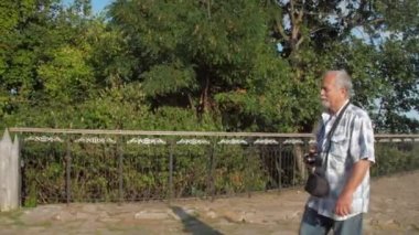 Boynunda kamera olan emekli bir adam sokakta yürümekten hoşlanıyor.