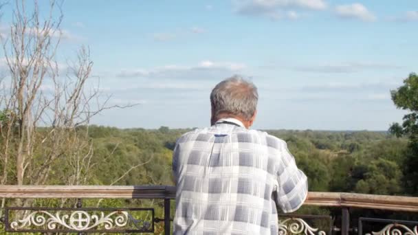 Vieil homme marche près de balustrade métallique contre la nature verte luxuriante — Video