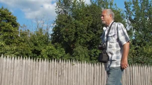 Pensiunan pria dengan kamera di leher menikmati berjalan di sepanjang jalan — Stok Video