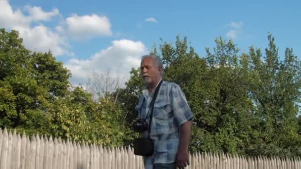 Homme retraité avec caméra sur le cou aime marcher le long de la rue — Video