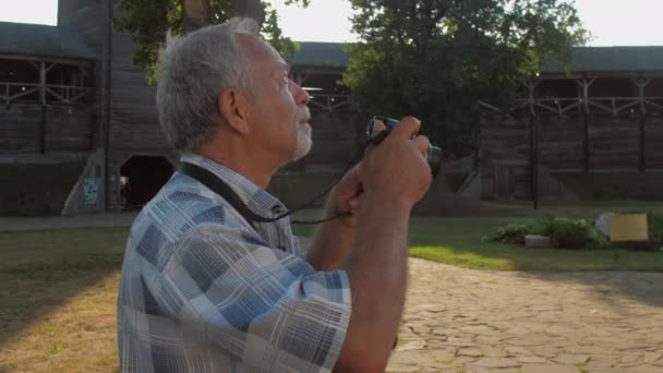 Пенсіонер тримає чорну камеру і фотографується в музейному парку — стокове відео