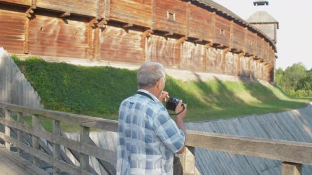 Пенсионер держит черную камеру и фотографируется в музейном парке — стоковое видео