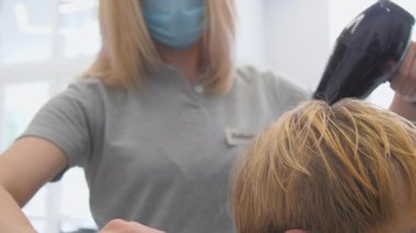 Kadın modern kurutucuyu elinde tutuyor ve erkeğin saçını tarıyor.