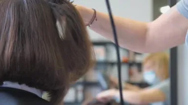 Yetenekli stilist eller kurutma makinesini tutar ve saç telini düzeltir.