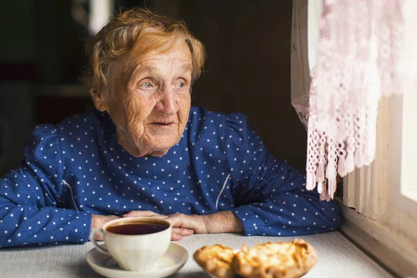 Old woman drinking tea with buns — Stock Photo, Image