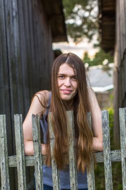Ahşap bir çit duran çekici genç uzun saçlı kadın.