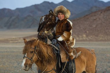 Sagsay, Moğolistan - 28 Eylül 2017: Genç kadına kartal avcı ise bir Altın Kartallar kollarını içinde çöl Dağ Batı Moğolistan üzerinde tutarak tavşan için avcılık geleneksel giyim.