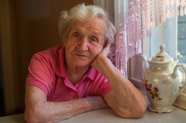 Yaşlı kadın masada çay içme portresi.