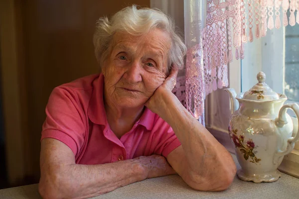 Yaşlı kadın masada çay içme portresi.