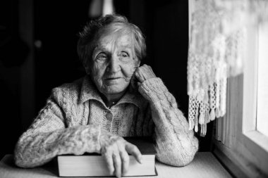 Yaşlı kadın ile pencerenin yakınındaki bir kitap.