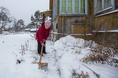 Yaşlı kadın kar köydeki evinin yakınında temizler.