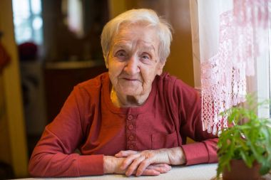 Evde masada oturan yaşlı bir kadın portresi.