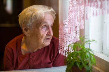 Older woman with longing looks out the window. clipart