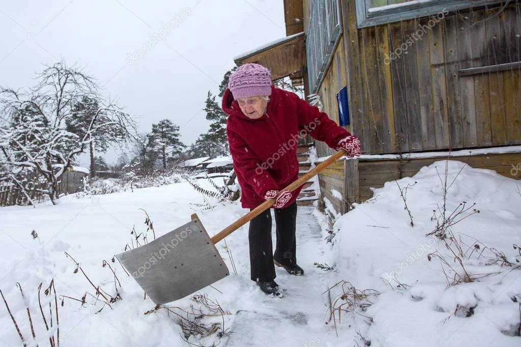 Elderly woman cleans the snow near rural home.