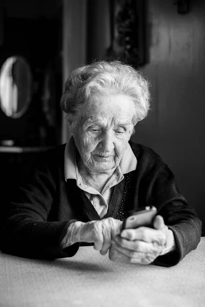 老妇人坐在家里的桌子上 拿着智能手机 黑白照片 — 图库照片