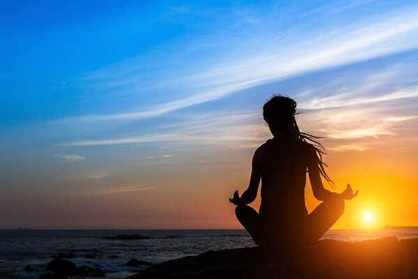 Yoga silhouette. Meditation woman on the ocean during amazing sunset. 