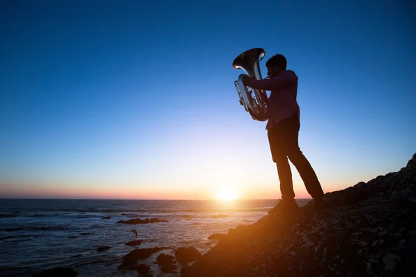 Silhouet Van Muzikant Met Tuba Rotsachtige Kust Tijdens Een Zonsondergang — Stockfoto