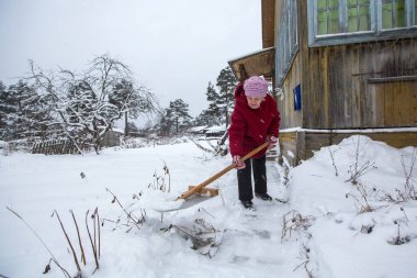 Yaşlı kadın kar evinizin yakınında temizler. Rusya.