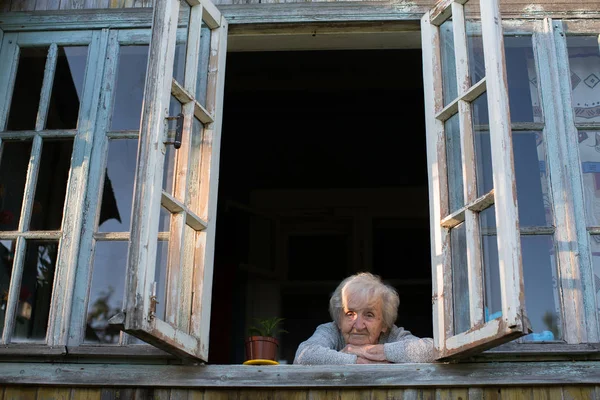高齢者の女性が村の家の窓から見える — ストック写真