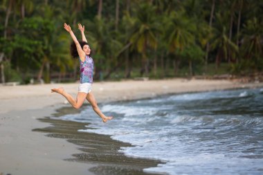 Genç kadın bir tropik sahilde denize atlar çalışır.