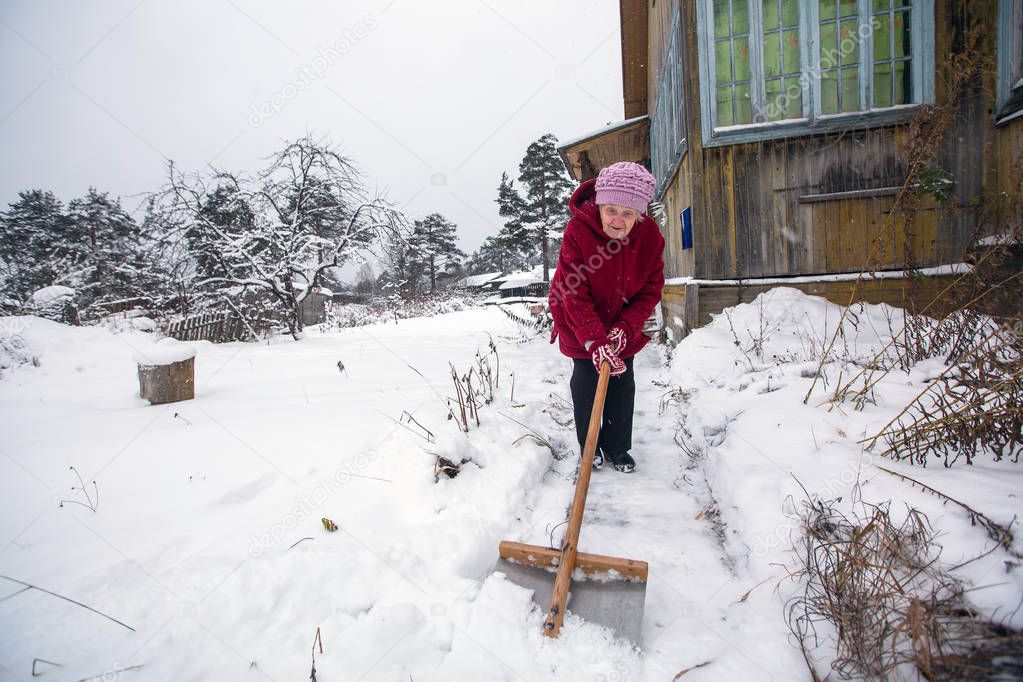 Elderly woman cleans the snow near rural home.