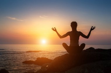 Pratik Yoga okyanus cliff sahilde günbatımı sırasında kadın siluet.