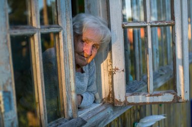 Yaşlı kadın bir köy evinin penceresinden görünüyor.