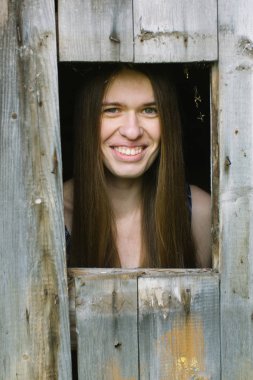 Genç kadın uzun saçlı ahşap kulübe pencereden görünüyor.