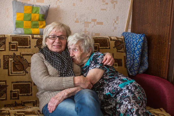老年妇女与她的成年女儿拥抱在沙发上 — 图库照片