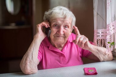 Yaşlı bir kadın evinde bir masada oturan bir cep telefonunda söz.