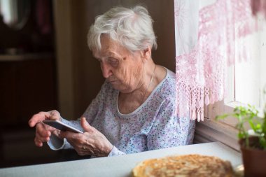 Yaşlı kadın bir smartphone ile onun elinde oturur..