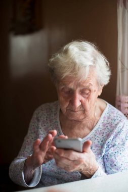 Yaşlı kadın bir smartphone ile onun elinde oturur..