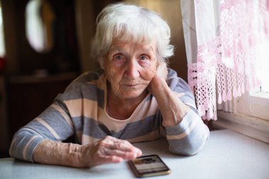 Yaşlı kadın akıllı telefonuyla masada oturuyor..