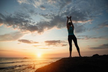 Fitness yogası yapan kadın gün batımında okyanusta egzersiz yapıyor..