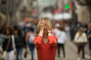 Halka açık bir yerde panik atak. Kalabalık caddede yürüyen insanlarla çevrili elleri ile gözlerini kapatan bir kadın.. 